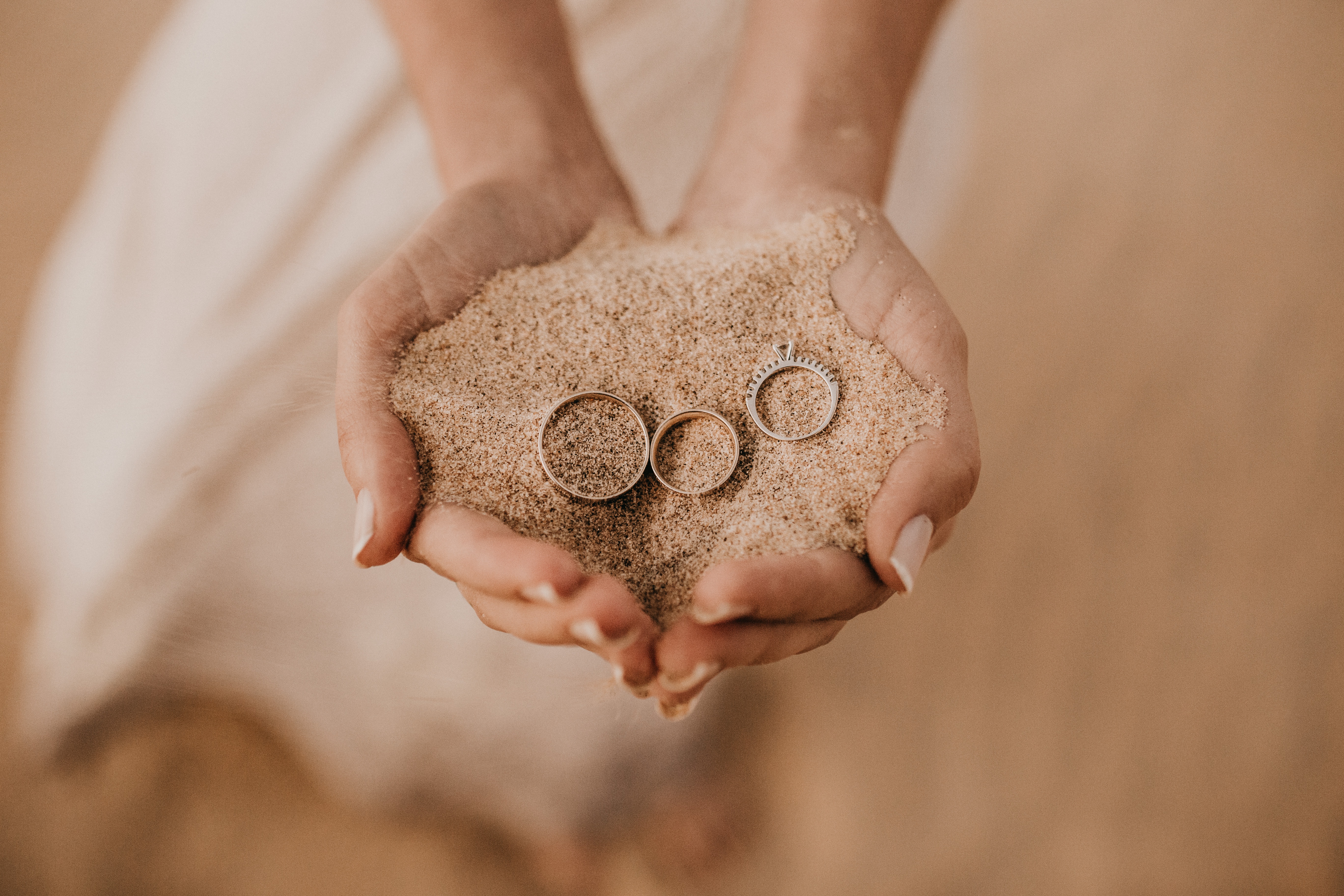 woman's hands holding sand and three wedding rings