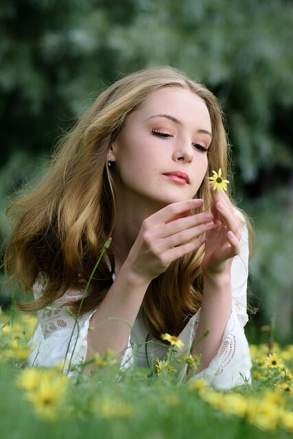 Blonde girl procrastinating while playing with a flower